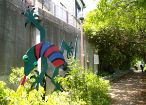 慶應ラグビー部グラウンド近くにある松の川緑道のシンボル・彫刻「爬虫類」ヤモリの像。「この道が、にんげんだけでなく、虫も鳥も、わしたち『爬虫類』も仲良く暮らせるような、楽しい草むらのある道になればと願っているんだ」との思いで設置された（2004年田辺光彰作）