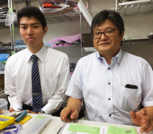 今年7月から新たに仲間に加わった新入社員の山口雅史さん（左）と、パソコン修理の作業スペースで。「部品一つも大切にしています」と、不具合の原因を徹底的に突き止めているという