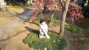 暖かそうな帽子をかぶって箒を持つ金蔵寺「小僧さんの像」（2020年12月、林宏美さん撮影）