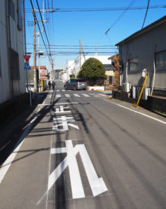 新吉田第二小学校西側交差点では道路の優先順位が変更となった。「止まれ」の道路標識を設置、道路に文字も新たに描き注意を喚起している。前方突き当りは御霊橋（ごりょうばし）方面（2月25日）