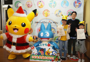 横浜日吉「下田地域ケアプラザ」にポケモンがやってきた！クリスマスの季節らしいサンタ衣装の「ピカチュウ」と記念撮影をおこなう「下田ほっと食堂」の参加者と山中市長（12月12日）