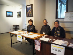 開催初日に来館者を出迎える大倉山エルムフォトクラブの高橋勲夫さん、徳武淳次さん、鶴谷典子さん（右より）