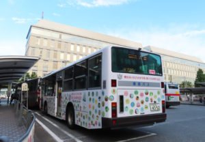 「日22系統」（日吉駅～サンヴァリエ日吉）を運行する日吉台小学校150周年記念のラッピングバス。後方は慶應大学日吉キャンパス協生館（7月6日）