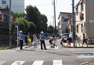 「高田東小学校前」交差点で児童を誘導する警察官。集団登校の児童たちが続々と登校していた