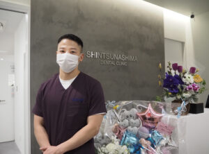 「新綱島デンタルクリニック歯科・矯正歯科」院長の田代慎（まこと）さん。スタイリッシュな内装の院内にたくさんのお祝いのお花たちが並んでいました