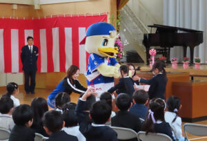 横浜F・マリノスのキャラクター「マリノスケ」とトリコロールマーメイズのさとみさん（右）、なぎささんからランドセルカバーが新1年生のクラス代表に贈呈された