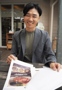 初めて考案した「新グランドメニュー」案を手に笑顔を浮かべる山田さん（5月24日）
