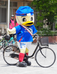 自転車の運転においても着用が義務化された「ヘルメット」を、「港北区安全安心大使」マリノスケもしっかりかぶって自転車の乗り方の見本を披露。港北警察署の担当者は、ボランティアで来訪していた保護者らにもヘルメットの着用を呼び掛けていた