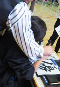 子どもたちの机を巡回、希望する児童と筆を一緒に進めるシーンも