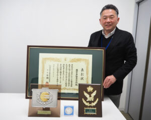 関東管区（10県）の警察局長と関東指定自動車教習所協会連合会会長からの表彰楯やメダル、全国指定自動車教習所連合会会長賞の表彰状や楯も。企画・広報を担当する加藤さんも「職員一人ひとりの力」が結集した結果としての受賞を喜ぶ