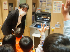 「ATMを見たことがある人」との問いかけに「はい！」と元気な挙手で回答する子どもたち